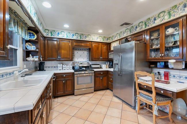 Kitchen with a sink, tile counters, stainless steel appliances, light tile patterned floors, and visible vents | Image 12