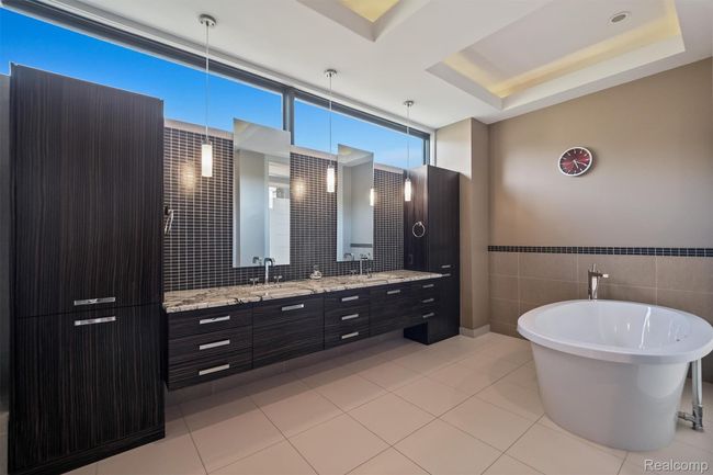 Bathroom with double vanity, a freestanding bath, tile walls, light tile patterned floors, and a tray ceiling | Image 21