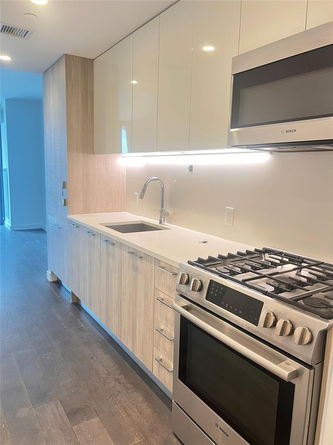 Kitchen featuring stainless steel appliances, modern cabinets, dark wood-style floors, and light countertops | Image 4