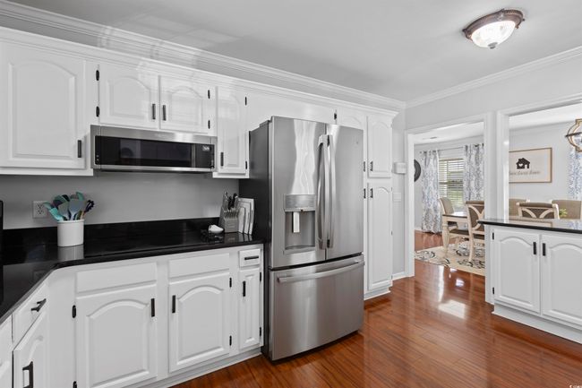 Kitchen with appliances with stainless steel finishes, dark countertops, white cabinetry, dark wood finished floors, and ornamental molding | Image 8