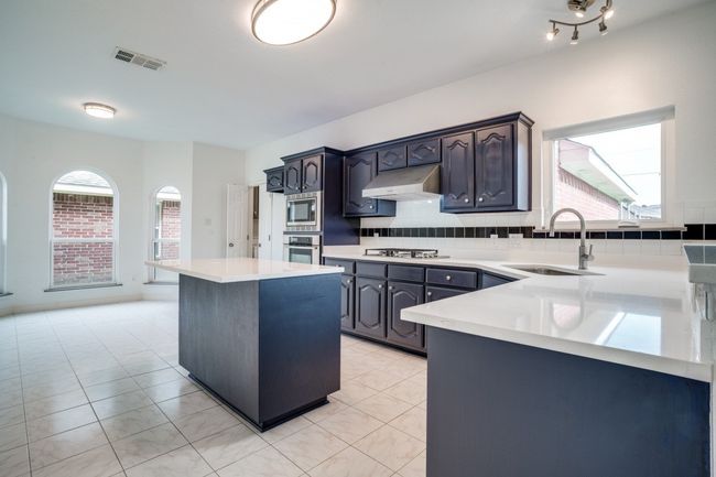 Kitchen featuring a sink, under cabinet range hood, appliances with stainless steel finishes, a center island, and light countertops | Image 8