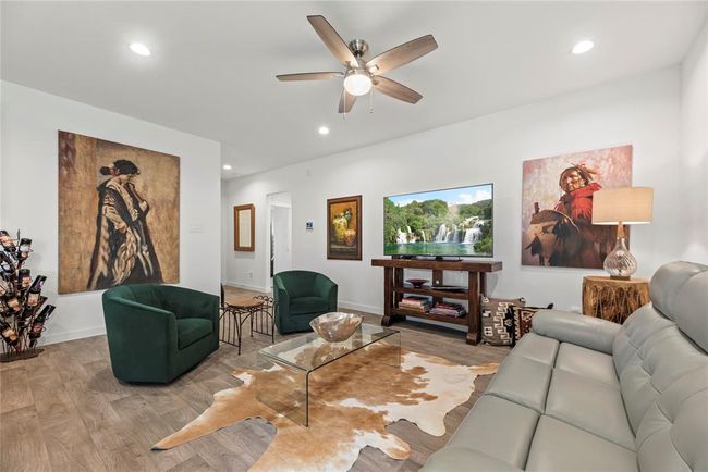 From this different angle, the living room reveals the hallway leading to the other rooms, offering a seamless flow throughout the home. The spacious layout still shines, with plenty of room for furniture and an open connection to the kitchen. The recessed lighting and ceiling fan continue to provide both ambiance and comfort, while the natural LVP floors run throughout, maintaining a consistent, warm feel across the space. | Image 6
