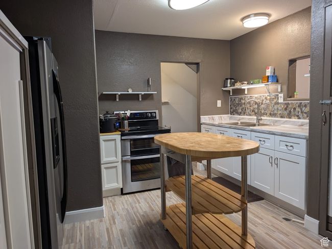 Kitchen featuring open shelves, a textured wall, appliances with stainless steel finishes, and a sink | Image 15