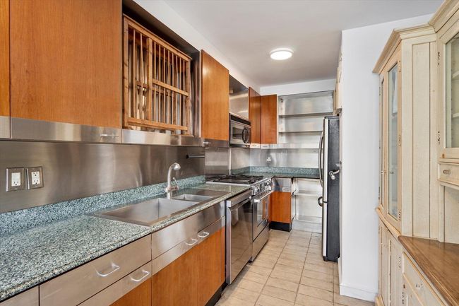 Kitchen with stainless steel appliances, light tile patterned floors, a sink, brown cabinets, and stone counters | Image 10
