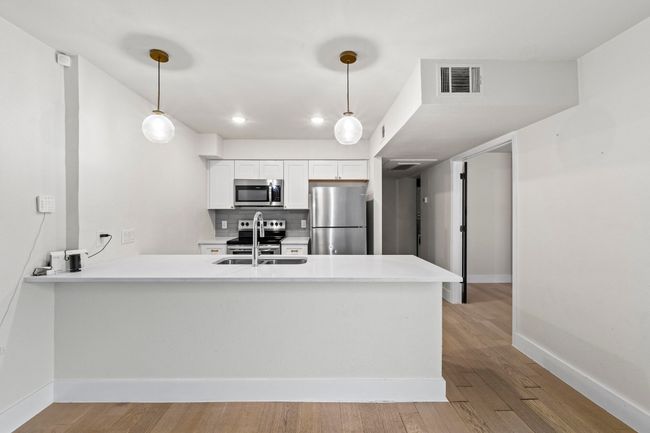 Kitchen with stainless steel appliances, a peninsula, baseboards, a sink, and light countertops | Image 30