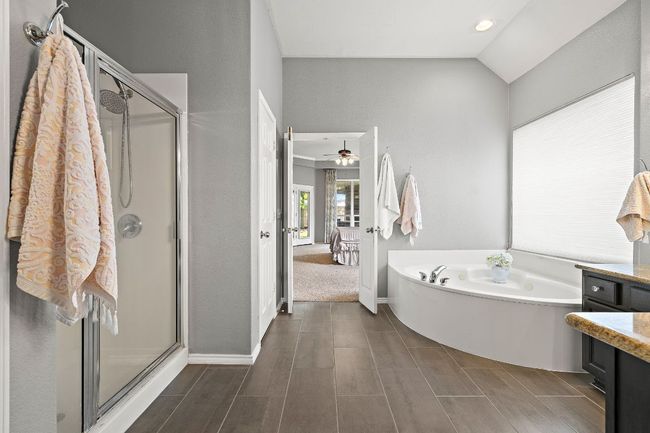 Full bath featuring a garden tub, a stall shower, lofted ceiling, vanity, and baseboards | Image 20