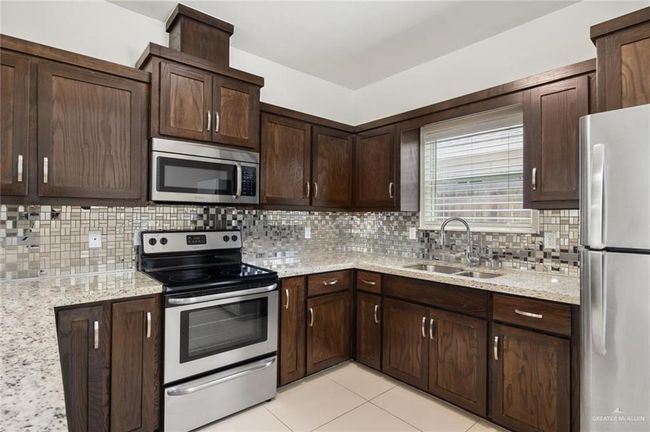 Kitchen featuring appliances with stainless steel finishes, a sink, tasteful backsplash, dark brown cabinets, and light tile patterned floors | Image 4