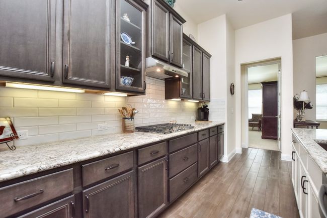 Kitchen featuring under cabinet range hood, backsplash, dark brown cabinets, and stainless steel gas cooktop | Image 7