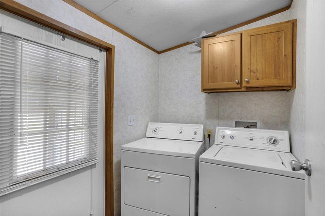 Laundry area featuring a textured ceiling, ornamental molding, washing machine and dryer, and cabinet space | Image 22