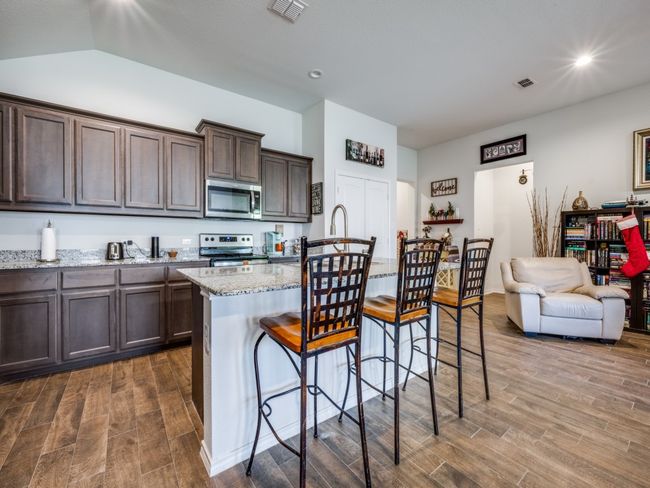 Kitchen featuring dark wood-style floors, dark brown cabinetry, appliances with stainless steel finishes, light stone countertops, and recessed lighting | Image 8