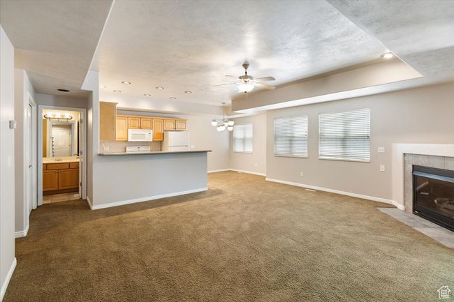 Open Living Area featuring carpet floors, a tiled fireplace, a chandelier, ceiling fan, and a raised ceiling | Image 6