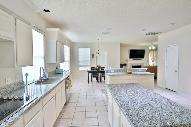 Kitchen with a center island, light tile patterned floors, stainless steel dishwasher, ceiling fan, and a fireplace | Image 7