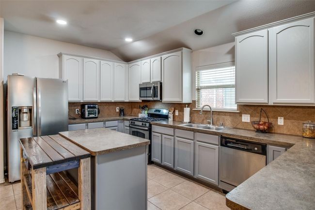 Kitchen with appliances with stainless steel finishes, a sink, light tile patterned floors, lofted ceiling, and decorative backsplash | Image 9