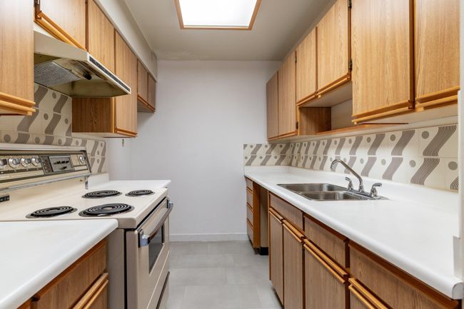 Kitchen with backsplash, a sink, light countertops, white range with electric stovetop, and under cabinet range hood | Image 11