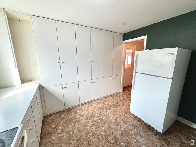 Kitchen with range, freestanding refrigerator, white cabinetry, stone finish flooring, and light countertops | Image 25