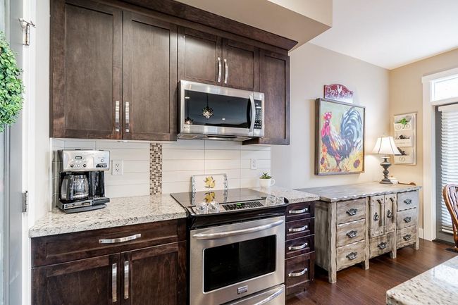 Kitchen featuring appliances with stainless steel finishes, dark brown cabinetry, dark wood-style floors, tasteful backsplash, and light stone countertops | Image 8