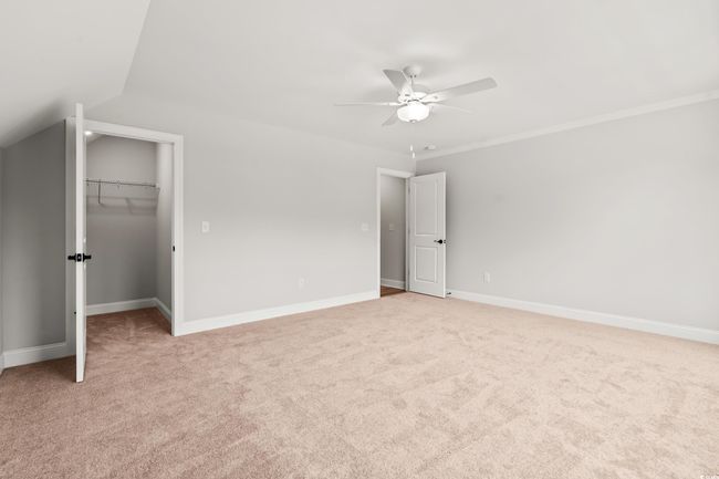 Unfurnished bedroom with light carpet, a walk in closet, baseboards, and lofted ceiling | Image 25