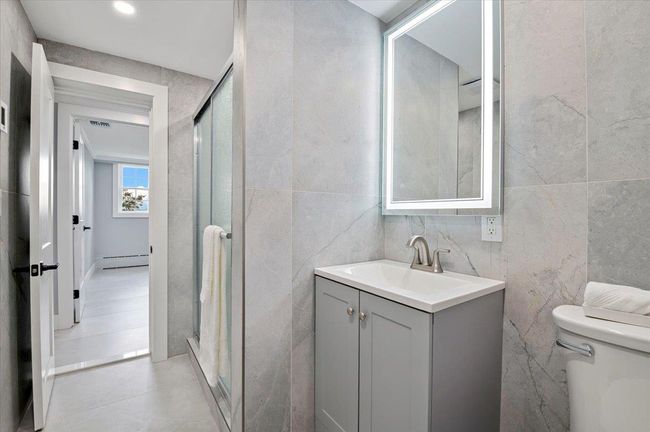 Bathroom with tile walls, vanity, a baseboard heating unit, and a shower stall | Image 28
