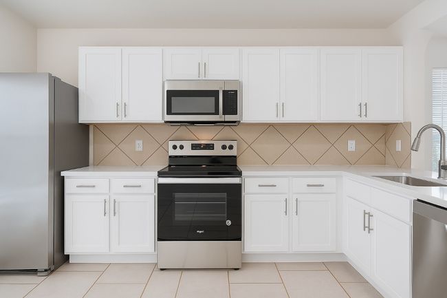 Kitchen featuring stainless steel appliances, a sink, white cabinets, light countertops, and tasteful backsplash | Image 4