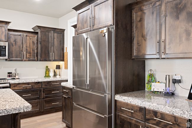 Kitchen with appliances with stainless steel finishes, dark brown cabinets, light stone countertops, and light wood-type flooring | Image 49