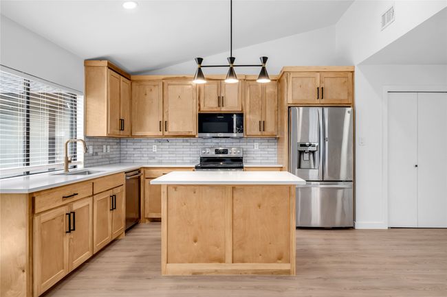 Kitchen featuring stainless steel appliances, light brown cabinets, a sink, lofted ceiling, and decorative backsplash | Image 13