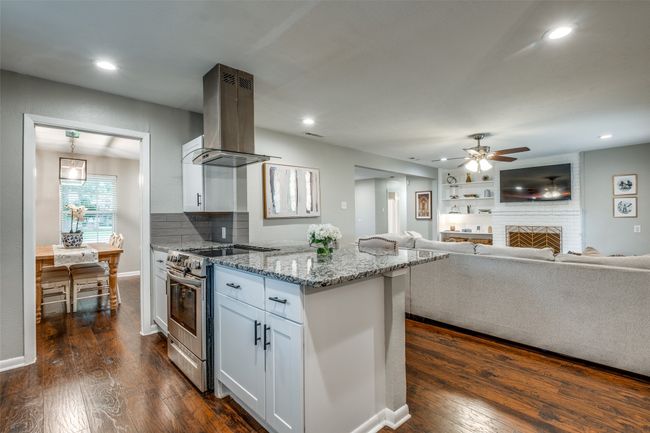 Kitchen with stainless steel range oven, island range hood, a ceiling fan, light stone counters, and white cabinets | Image 19