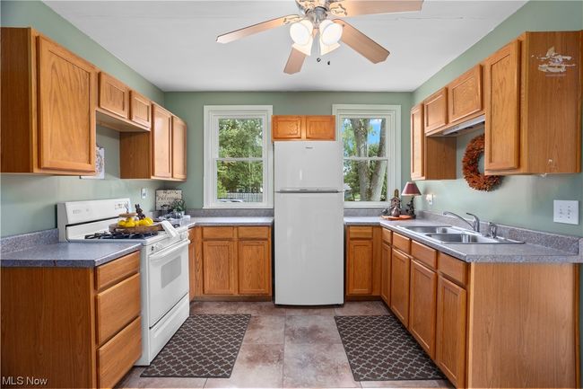 Kitchen featuring brown cabinets, light countertops, light tile floors, ceiling fan, and white appliances | Image 4