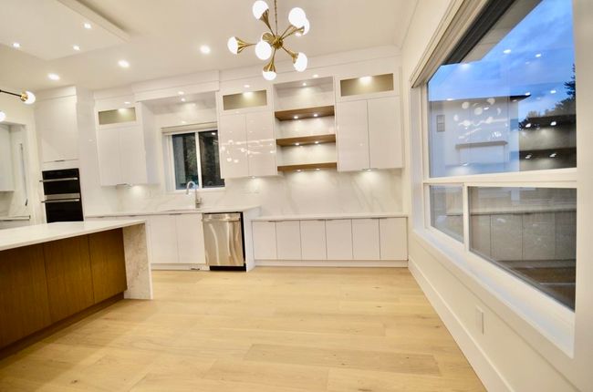 Kitchen featuring stainless steel appliances, modern cabinets, white cabinetry, a chandelier, and light wood-style flooring | Image 16