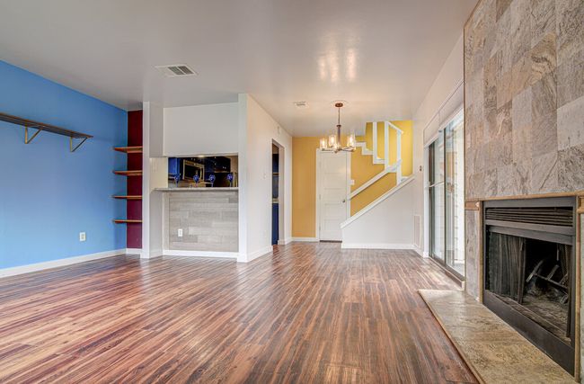 Unfurnished living room featuring visible vents, a chandelier, wood finished floors, a tiled fireplace, and baseboards | Image 5