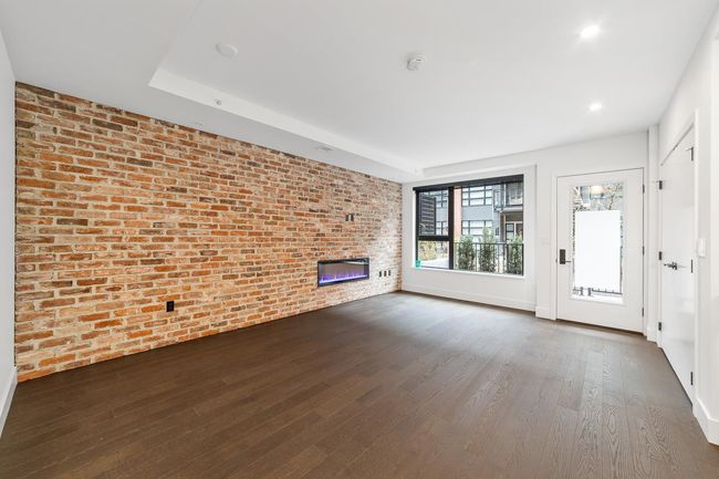 Unfurnished living room with brick wall, a glass covered fireplace, dark wood-type flooring, and recessed lighting | Image 16