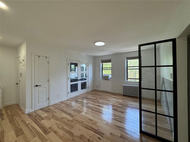 Empty room with radiator heating unit, french doors, light wood finished floors, and cooling unit | Image 7