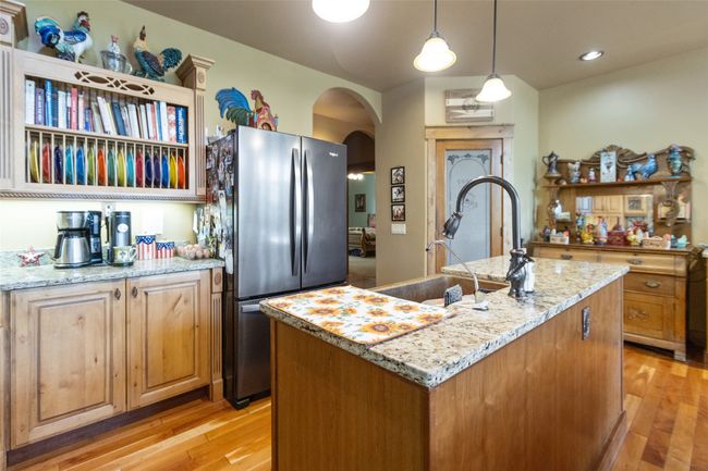 Kitchen featuring freestanding refrigerator, arched walkways, light wood-style flooring, a kitchen island with sink, and light stone countertops | Image 15