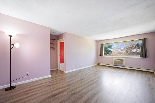 Unfurnished living room with an AC wall unit, baseboards, wood finished floors, and a baseboard radiator | Image 9