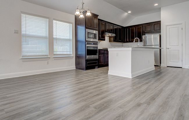 Kitchen featuring stainless steel appliances, under cabinet range hood, backsplash, light wood-type flooring, and a chandelier | Image 11