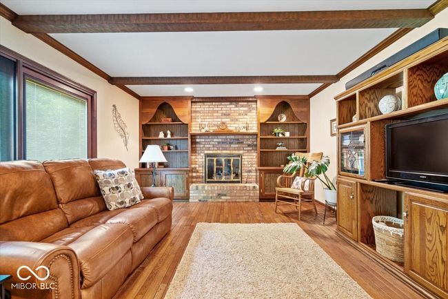 living room with beamed ceiling, light wood finished floors, a fireplace, crown molding, and recessed lighting | Image 8