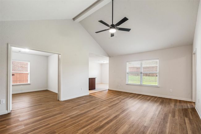 Unfurnished living room with beam ceiling, a ceiling fan, wood finished floors, high vaulted ceiling, and baseboards | Image 6