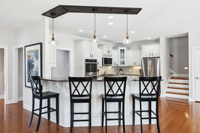 Light-filled kitchen with white cabinetry, granite countertops, and seating for four at the peninsula. | Image 6