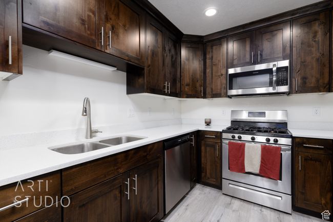 Kitchen featuring a sink, dark brown cabinets, light wood-type flooring, and appliances with stainless steel finishes | Image 14