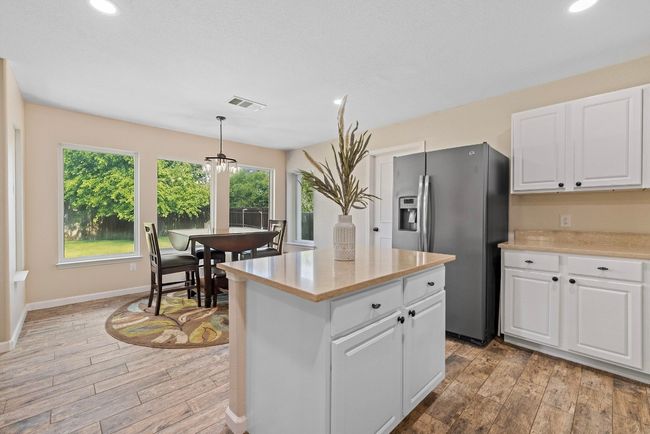 Kitchen featuring stainless steel fridge with ice dispenser, light wood-type flooring, light countertops, white cabinetry, and recessed lighting | Image 8