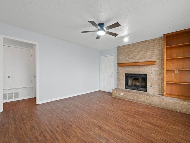 Unfurnished living room featuring ceiling fan, a textured ceiling, dark wood-type flooring, and a fireplace | Image 6