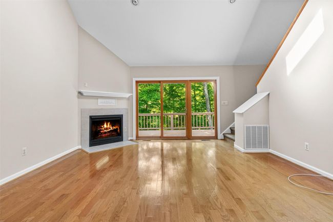 Unfurnished living room with a fireplace, vaulted ceiling, wood finished floors, baseboards, and stairway | Image 4