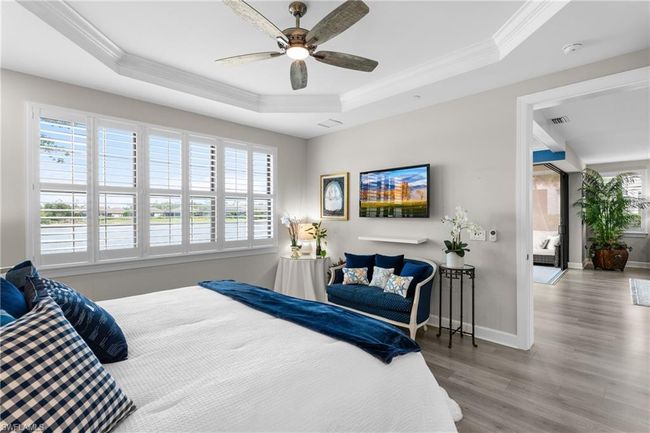 Bedroom featuring a tray ceiling, multiple windows, crown molding, wood finished floors, and a ceiling fan | Image 17