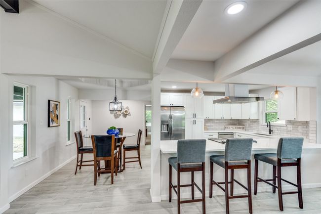 Kitchen featuring a breakfast bar, a peninsula, backsplash, white cabinetry, and decorative light fixtures | Image 15