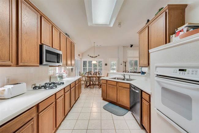Kitchen with appliances with stainless steel finishes, a sink, lofted ceiling, light tile patterned floors, and light countertops | Image 15