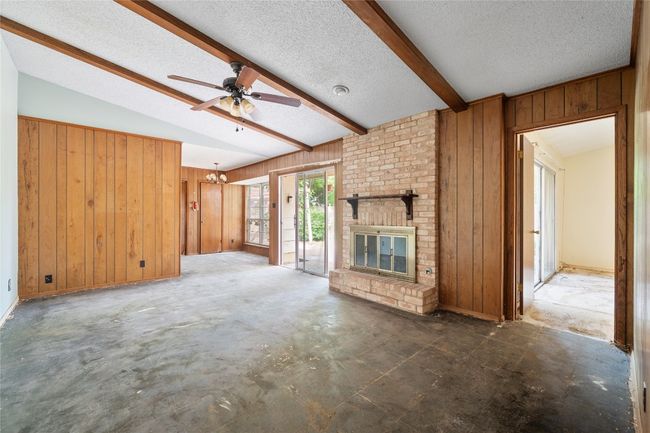 Unfurnished living room with wooden walls, a textured ceiling, a ceiling fan, a fireplace, and concrete floors | Image 6