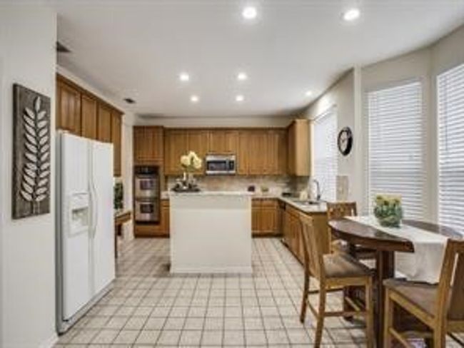 Kitchen featuring appliances with stainless steel finishes, a center island, brown cabinetry, recessed lighting, and light countertops | Image 8