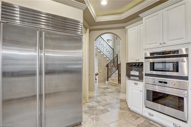 Kitchen featuring dark stone counters, white cabinetry, ornamental molding, arched walkways, and appliances with stainless steel finishes | Image 19