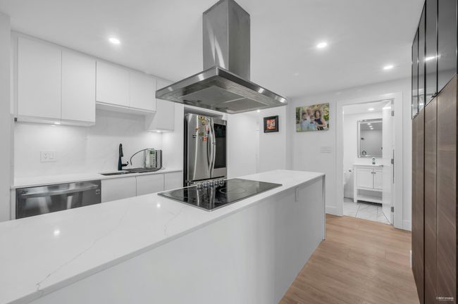 Kitchen featuring island exhaust hood, stainless steel appliances, white cabinets, and a sink | Image 16