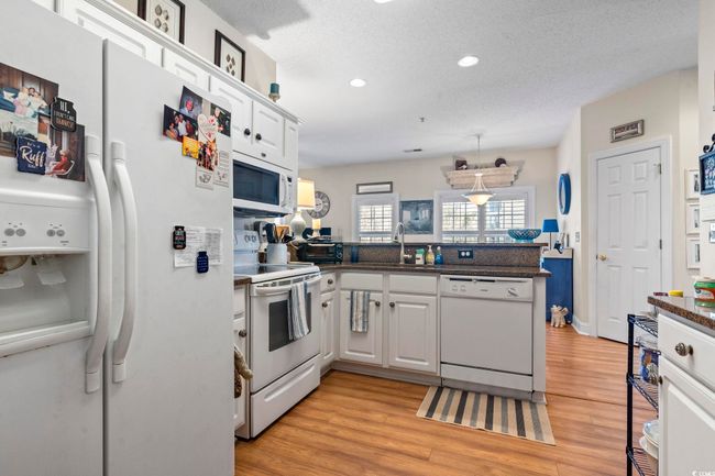 Kitchen with a sink, white cabinetry, a peninsula, light wood-style flooring, and white appliances | Image 10