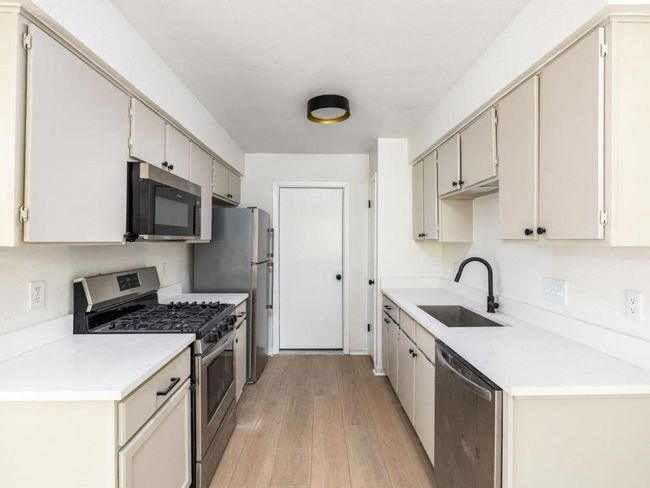 Kitchen featuring appliances with stainless steel finishes, a sink, light wood finished floors, and light countertops | Image 9